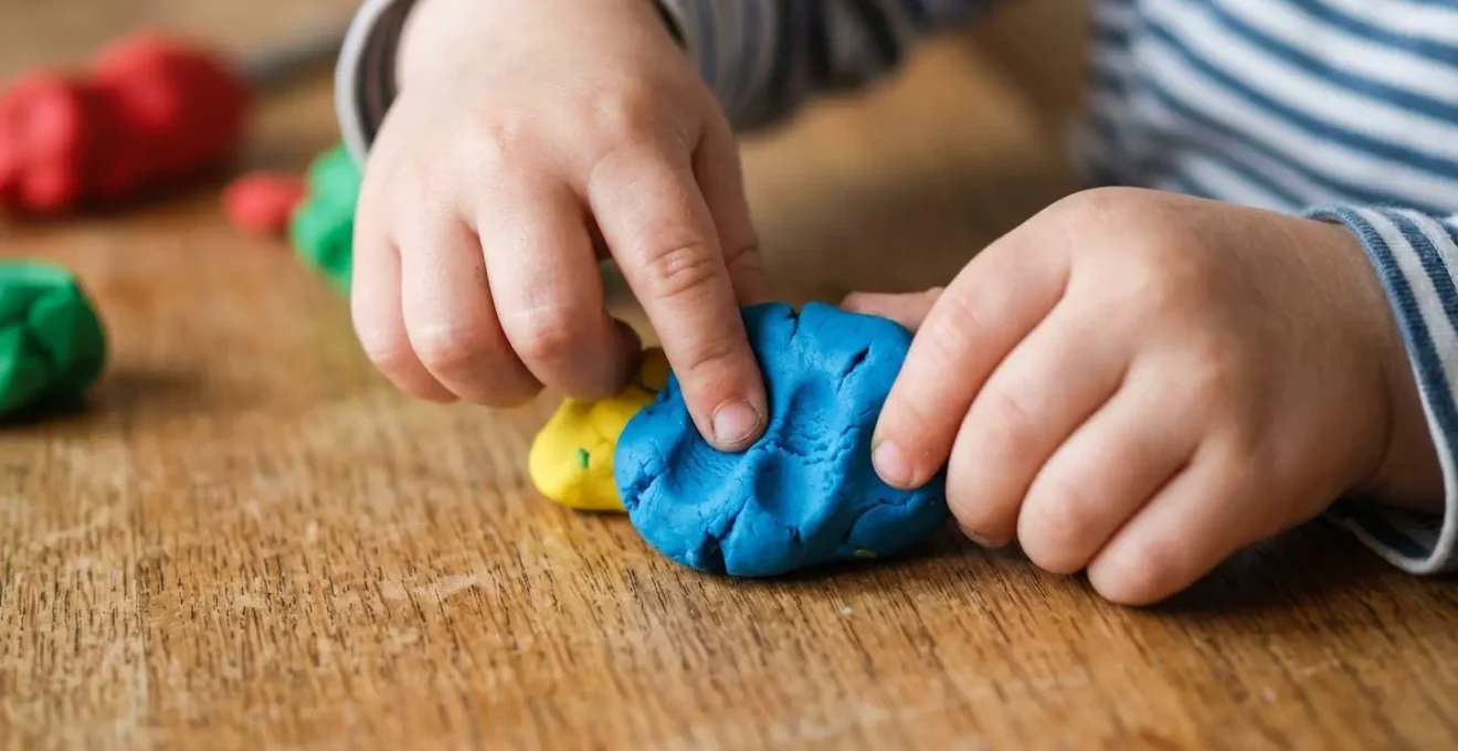 Mains d'un jeune enfant manipulant de la pâte à modeler pour développer la motricité fine en préparation au découpage