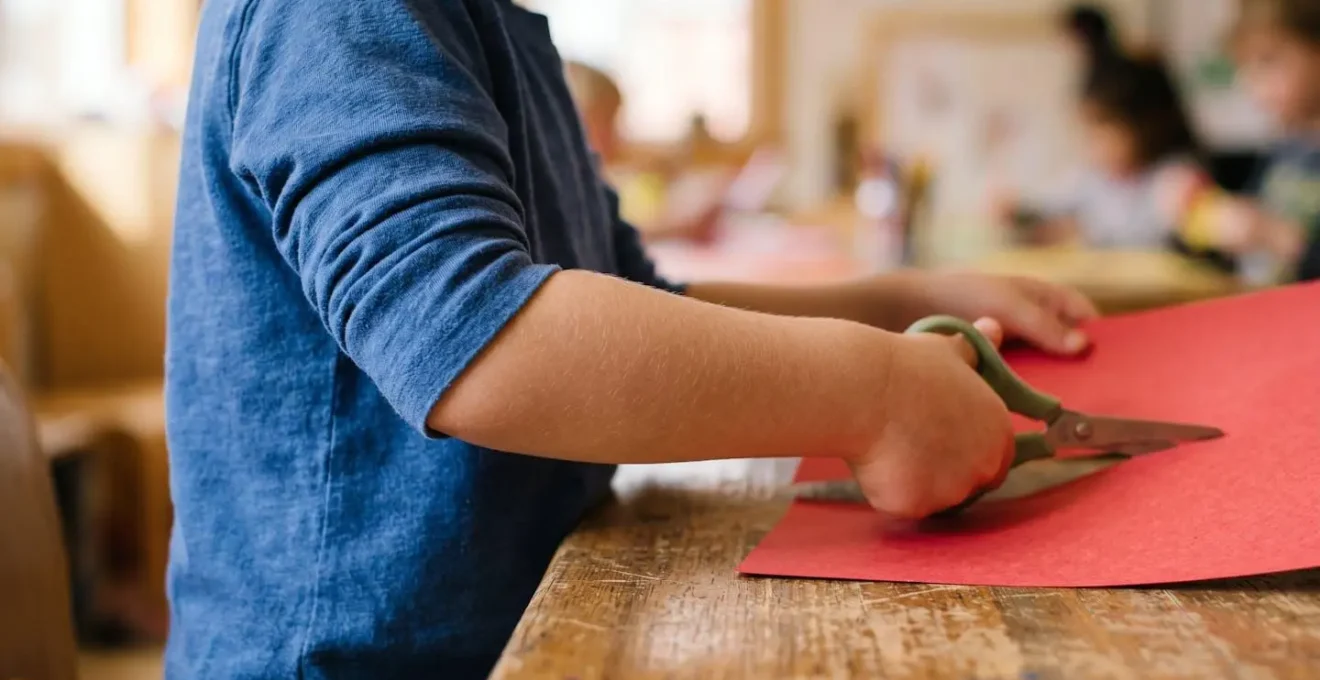 Détail des mains et bras d'un enfant montrant la position ergonomique correcte du coude près du corps lors du découpage