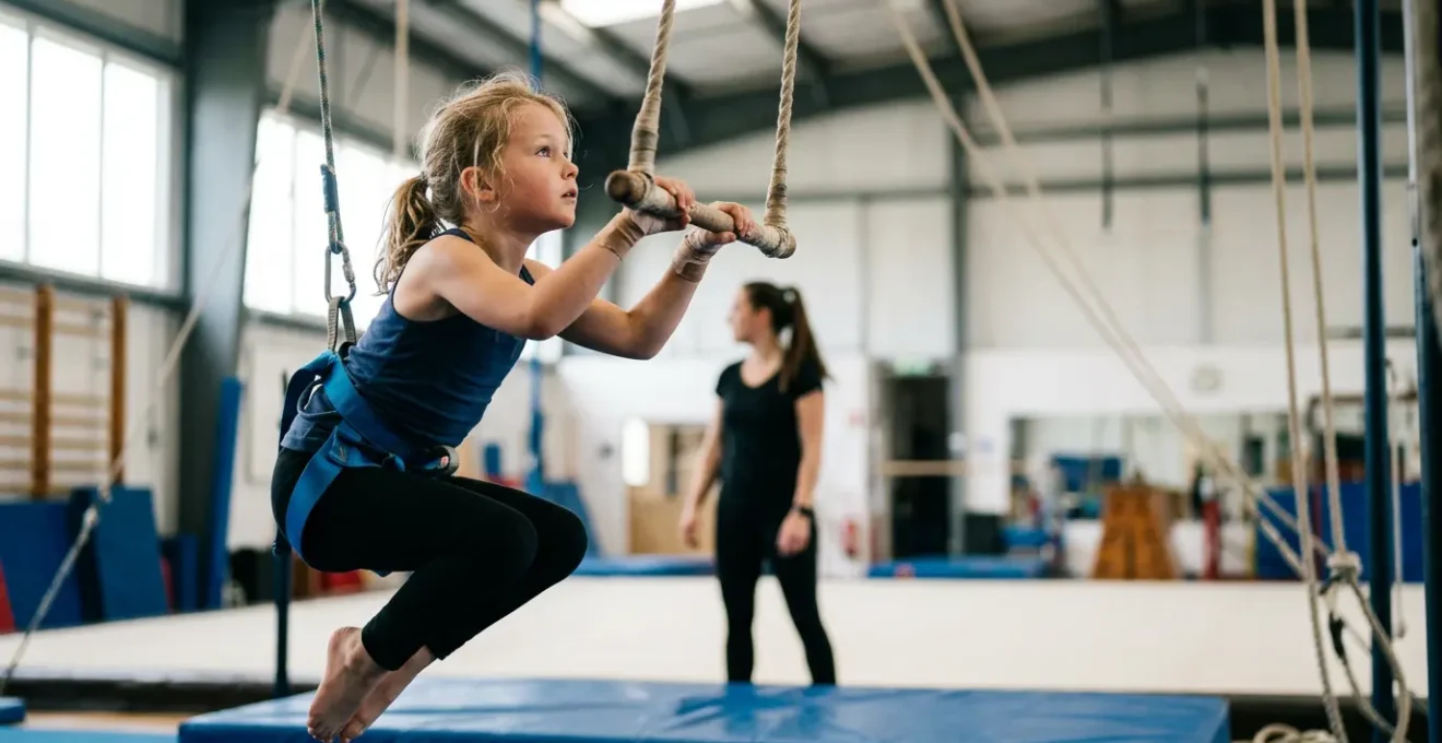 Enfant pratiquant le trapèze dans un cours de cirque, soutenu par un système de sécurité